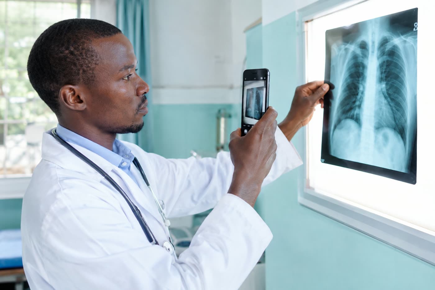 A doctor photographing an X-ray film on a lightbox with a smartphone